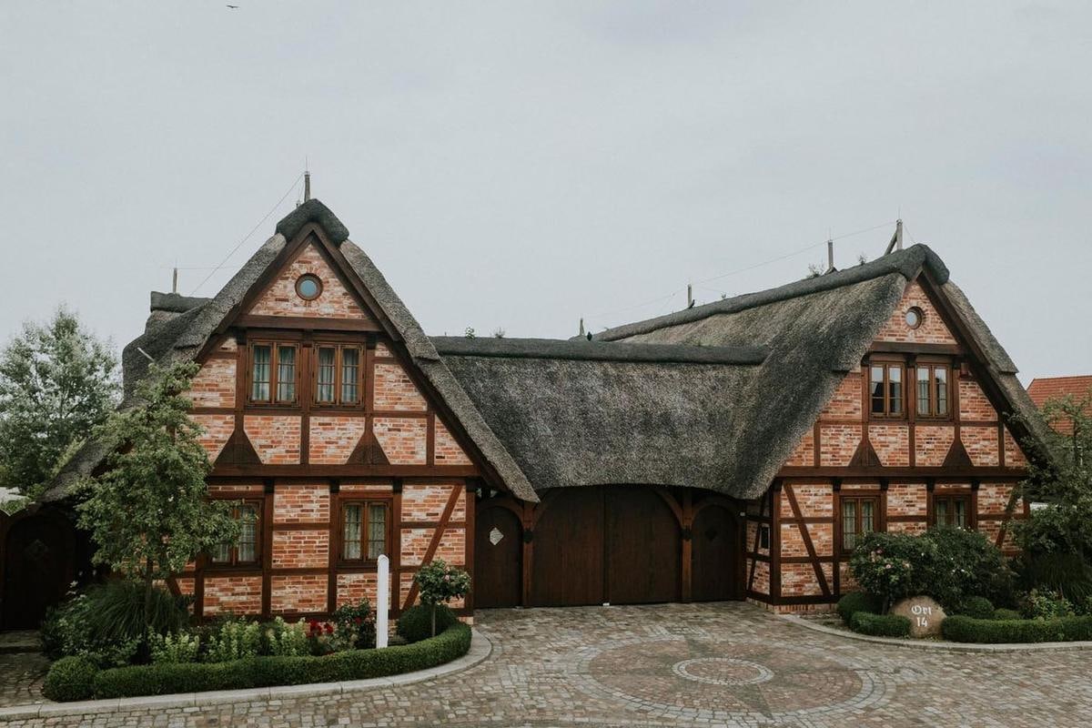 Breites Fachwerkhaus mit Reetdach und Vorplatz.
