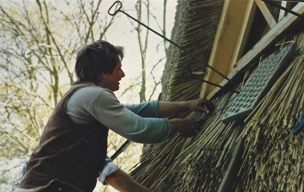 Ein junger Mann arbeitet mit Werkzeug an einer Reetfläche.